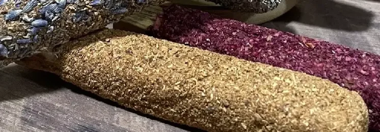 Getrocknete Kräuter und Blüten in Reihen: grüne, beige und dunkelrote Häufchen auf grauem Untergrund.