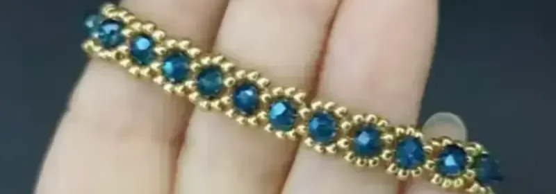 Hand mit goldenem Armband, besetzt mit blauen facettierten Steinen in regelmäßigem Muster.