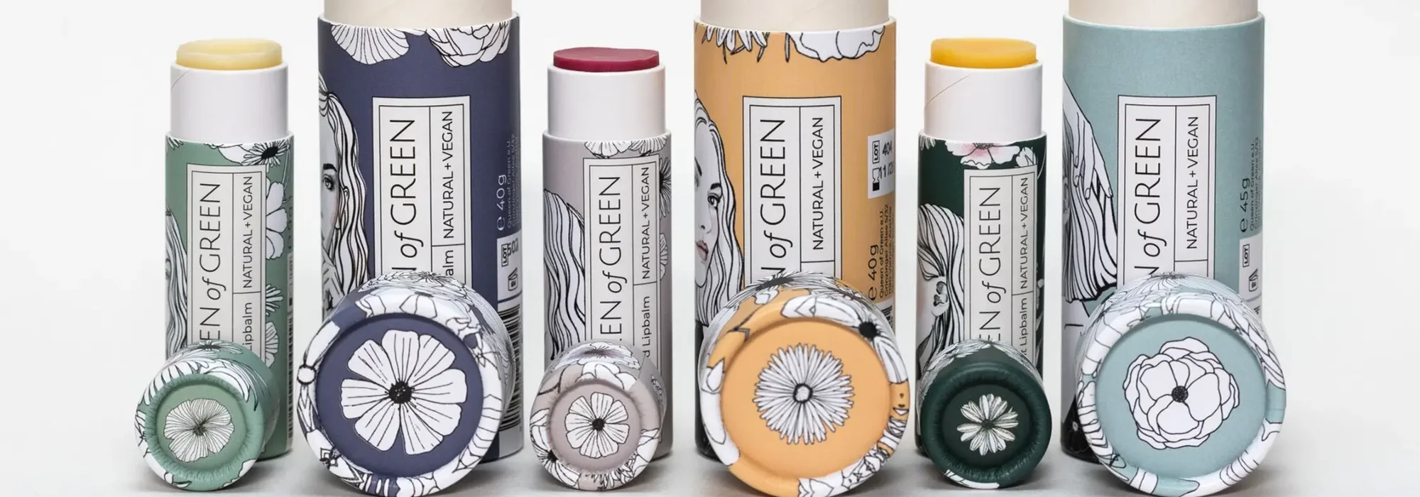 Sechs Lippenbalsam-Stifte in Papierhülsen mit Blumenzeichnungen, in Grün, Blau, Grau, Orange und Hellblau, nebeneinander…