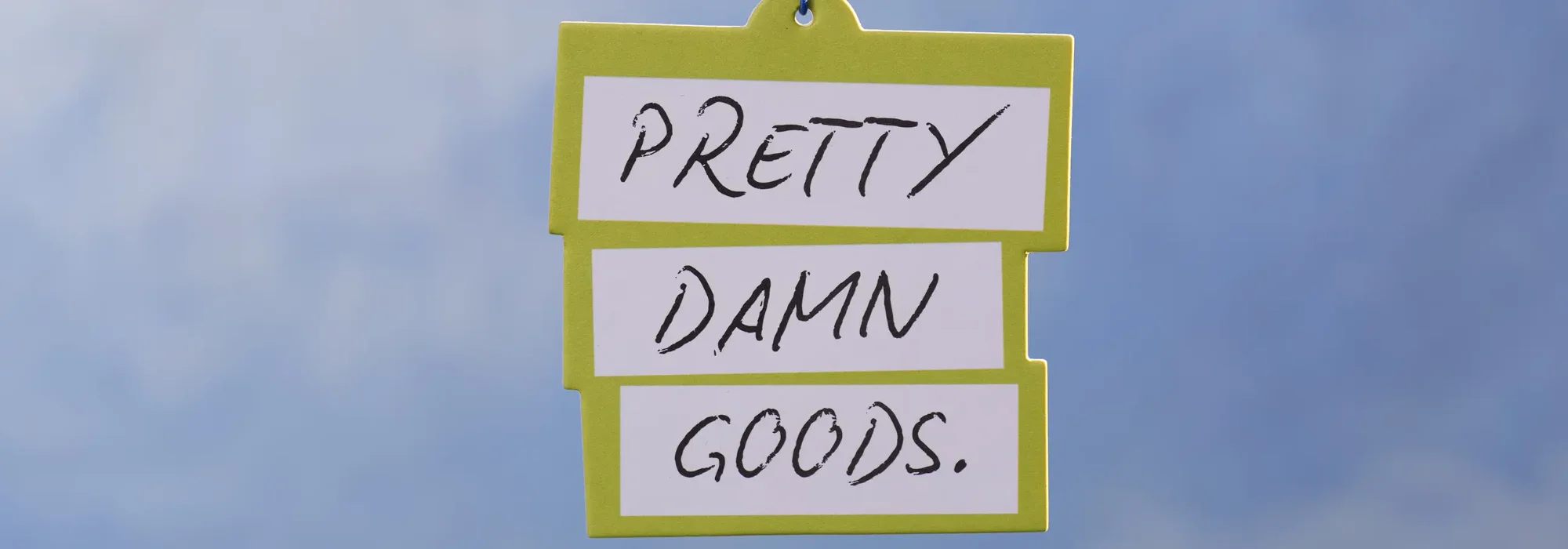 Grünes Schild mit drei weißen Feldern, handschriftlich beschriftet mit „PRETTY DAMN GOODS.