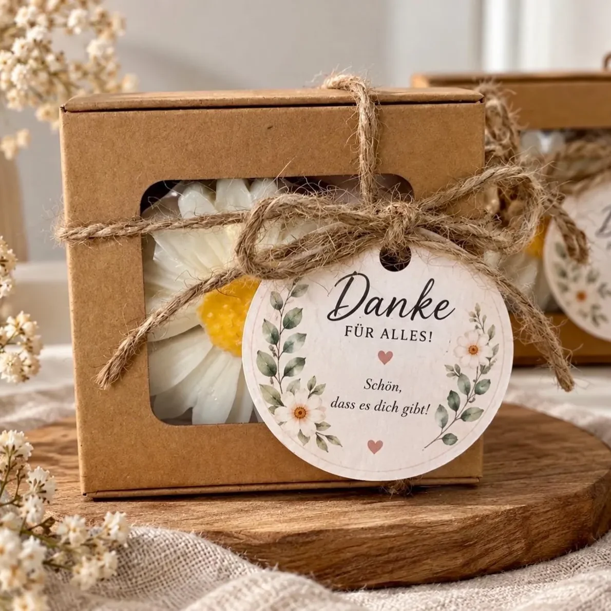 Kerze Gänseblümchen in weißer Blütenform, verpackt in Kraftkarton mit Sichtfenster, Juteband und Geschenkanhänger