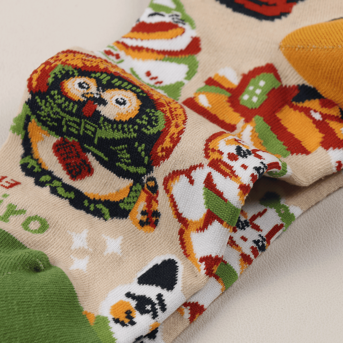 Nahaufnahme von Baumwollsocken mit bunten Glücksbringer-Puppen in Rot, Grün, Orange und Schwarz auf Creme-Grund…