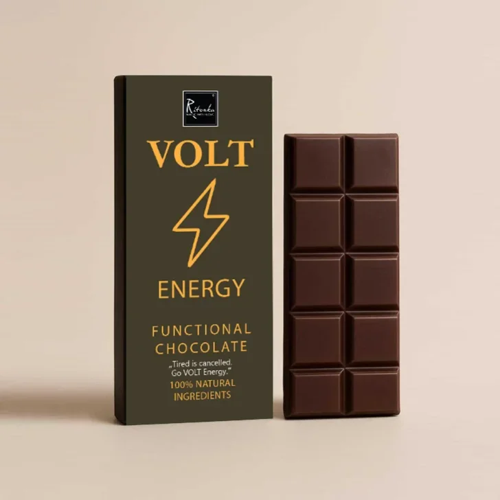 Schokolade mit Koffein: Dunkelgrüne Verpackung mit goldenem VOLT-Blitz-Logo neben aufgebrochener Zartbitterschokolade in…