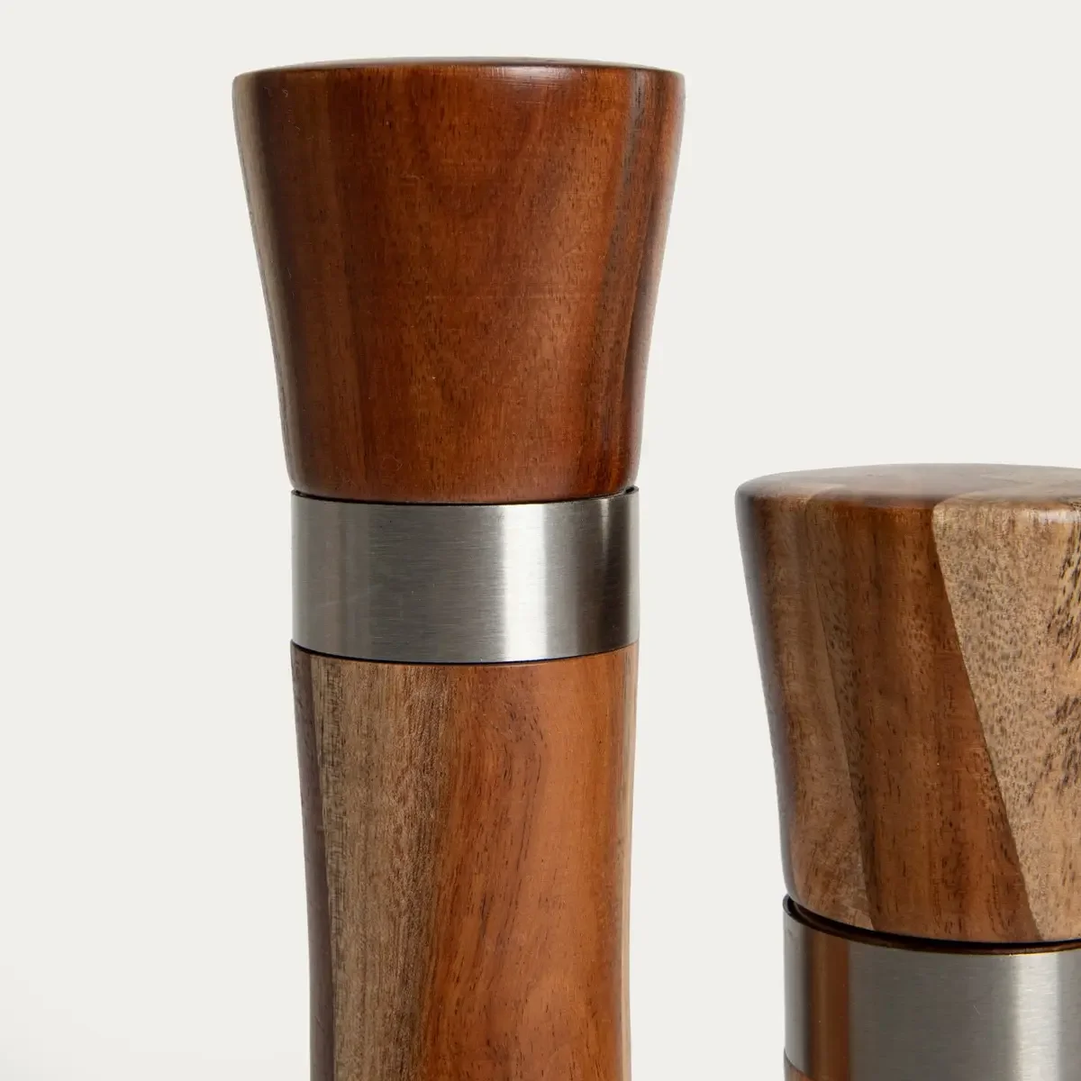 Zwei Holzmühlen nebeneinander, die größere links mit dunkelbraunem Holz und Aluminiumband, die kleinere rechts mit hellerem…