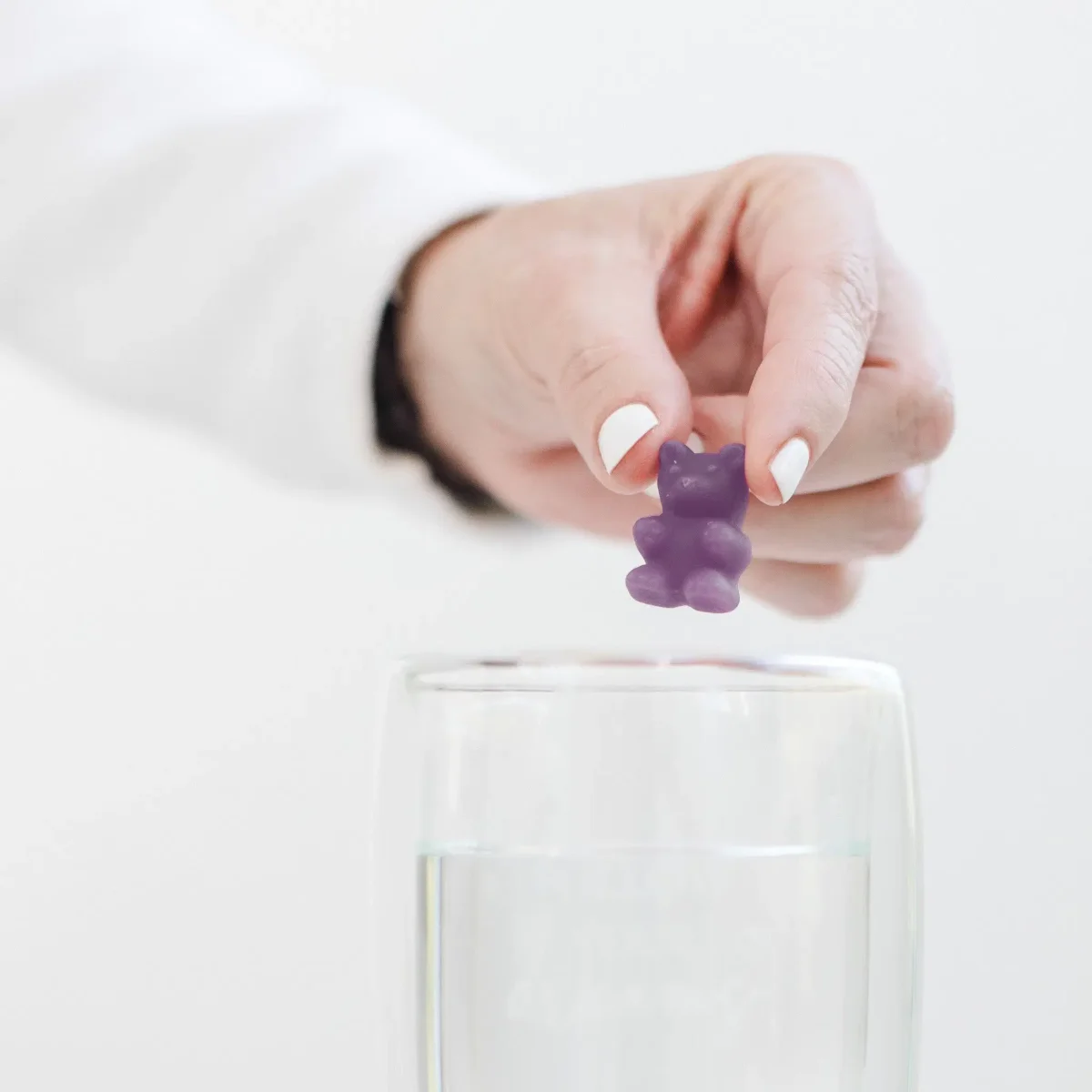 Hand hält violettes Teebärli über ein Glas mit heißem Wasser
