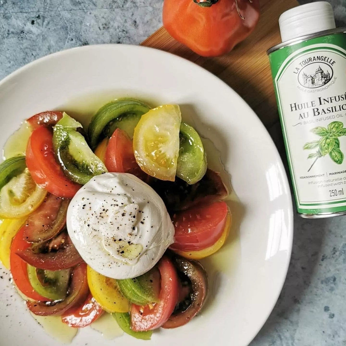 Farbenfroher Tomatensalat mit Mozzarella in weißer Schale, daneben die grüne Flasche Basilikum-Öl von La Tourangelle.