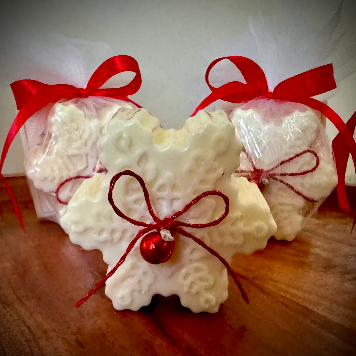Kerze Schneeflocke aus Sojawachs, weiß, mit roten Schleifen und Christbaumkugel, in Tüll verpackt.