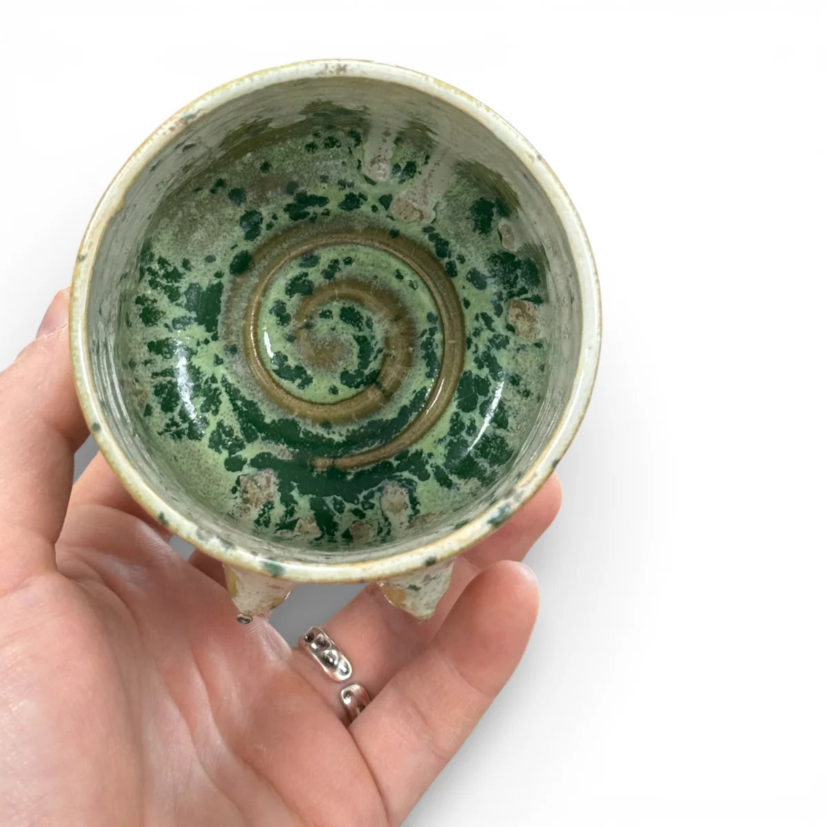 Blick von oben in einen grün-goldenen Keramikbecher mit strukturierter Glasur und konzentrischen Ringen, in einer Hand…