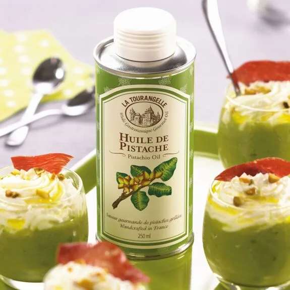 Pistazienöl-Flasche von La Tourangelle mit grünem Etikett, umgeben von Salatschüsseln und Besteck auf hellem Untergrund.