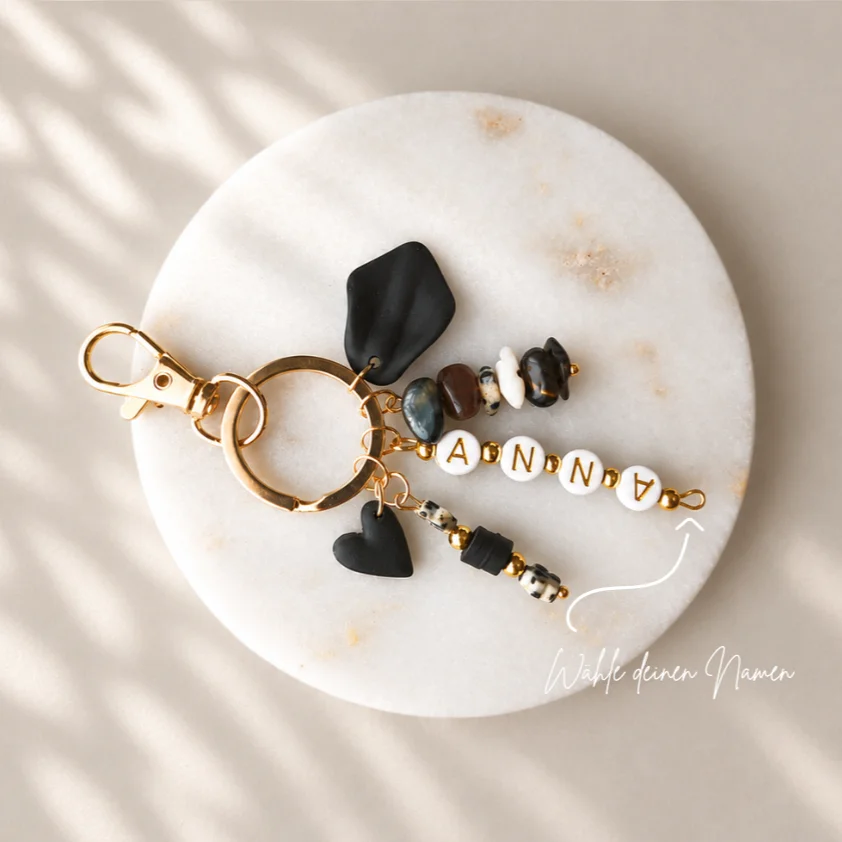 Schlüsselanhänger mit Namen ANNA auf weißen Buchstabenperlen, goldener Ring, schwarze Polymer-Anhänger und Natursteinperlen…