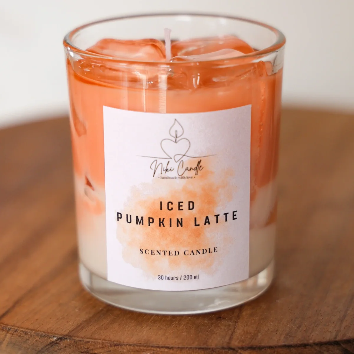 Duftkerze Pumpkin Latte in Glasgefäß mit orangefarbenem Wachs und sichtbaren Eiswürfeln, Etikett von vorne
