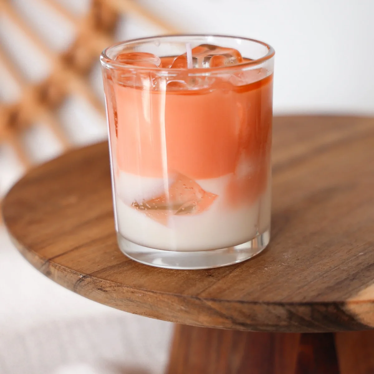 Kerze im Glas mit orangebrauner Flüssigkeit oben und cremefarbener Wachsschicht unten, realistische Eiswürfel oben, auf…