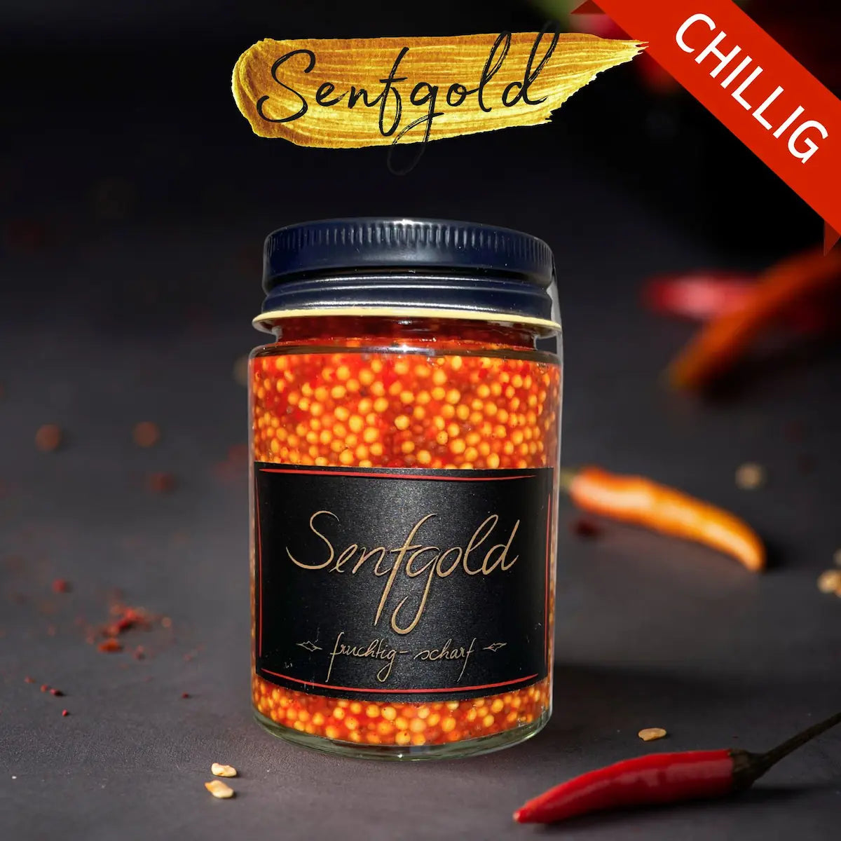 Senfkaviar im Glas: goldgelbe und rötliche Senfkörner hinter schwarzem Etikett, daneben rote Chilischoten auf dunklem…