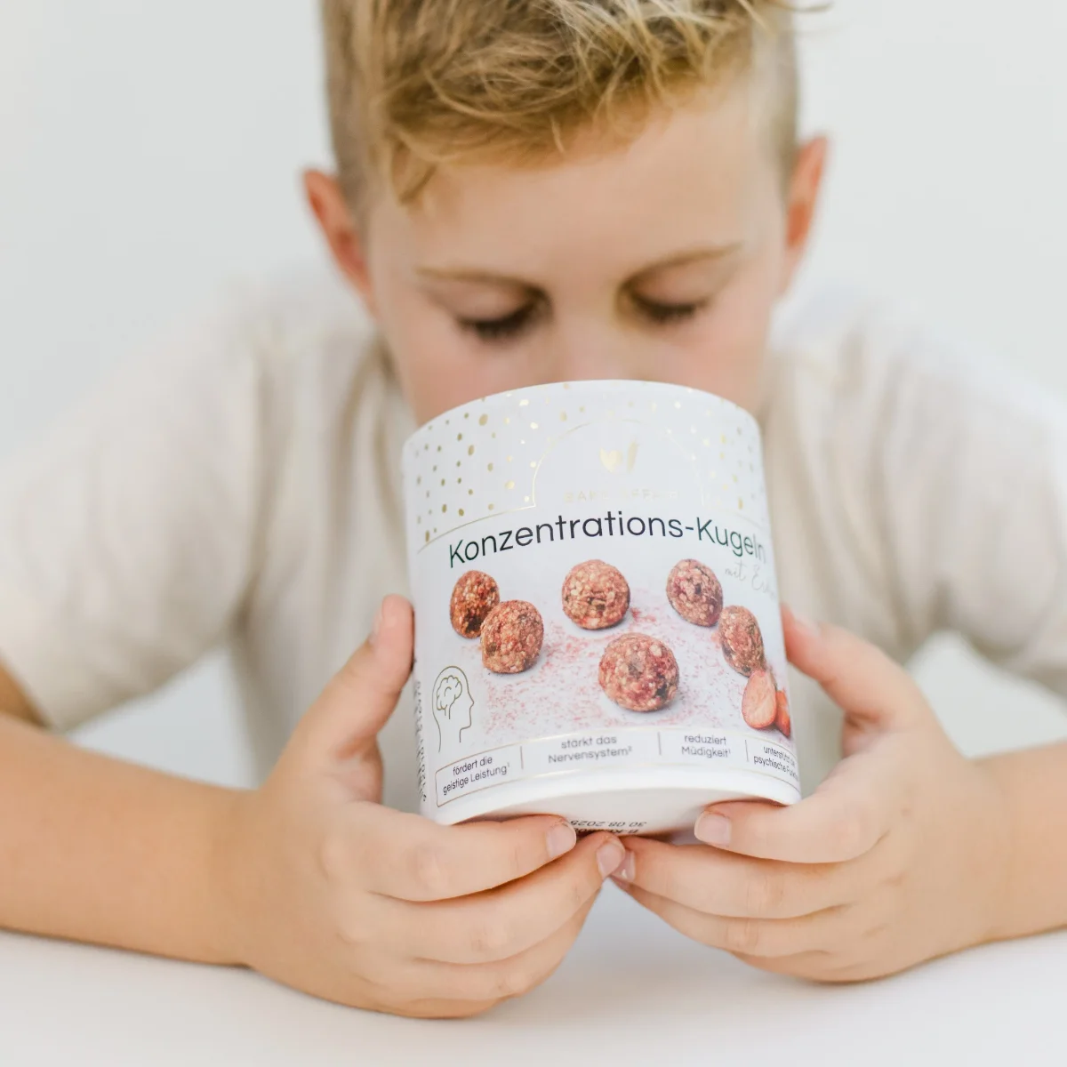 Kind hält Verpackung der Konzentrations-Kugeln in beiden Händen, Blick auf die bedruckte Vorderseite mit Produktfotos.