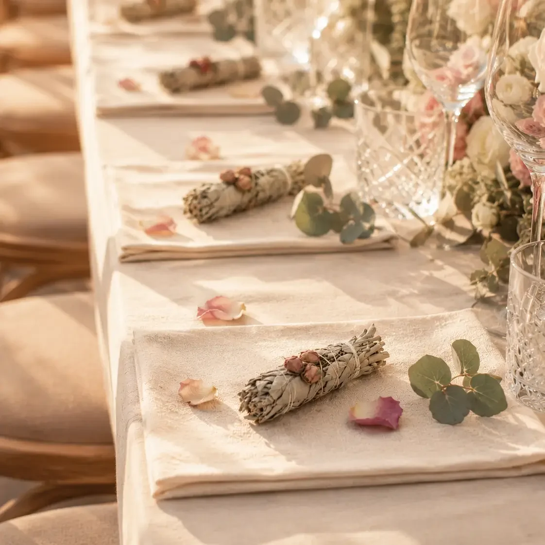 Mehrere Salbei-Rosenknospen-Bündel auf weißem Papier, umgeben von getrockneten Rosenblättern und Eukalyptuszweigen.