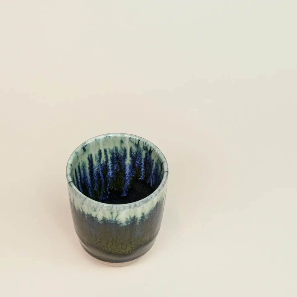 Henkellose Keramiktasse von oben aus leichter Schräge, Innenseite mit blauen Laufspuren über mintgrüner Glasur, auf…