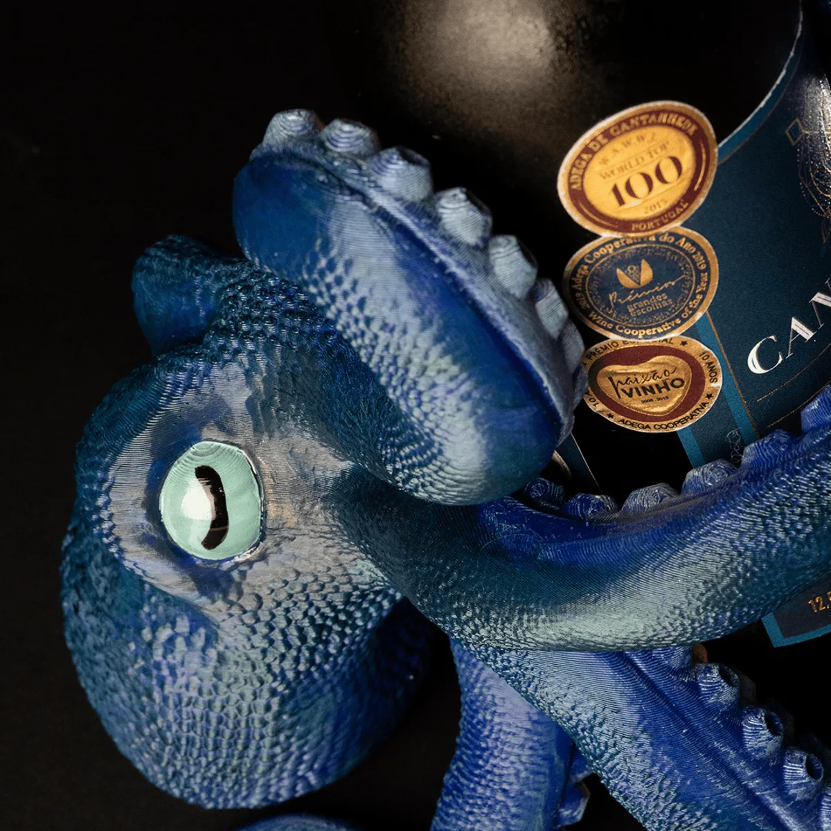 Blaubemalter Kraken-Flaschenhalter von oben, eine Flasche mit Medaillen in einer Tentakel, detailliertes Auge sichtbar.