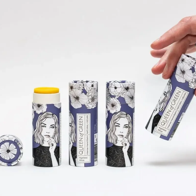 Drei violette Papphülsen mit Blumenmuster und Frauenporträt, daneben ein geöffneter Stick mit gelbem Deckel; eine Hand hält…