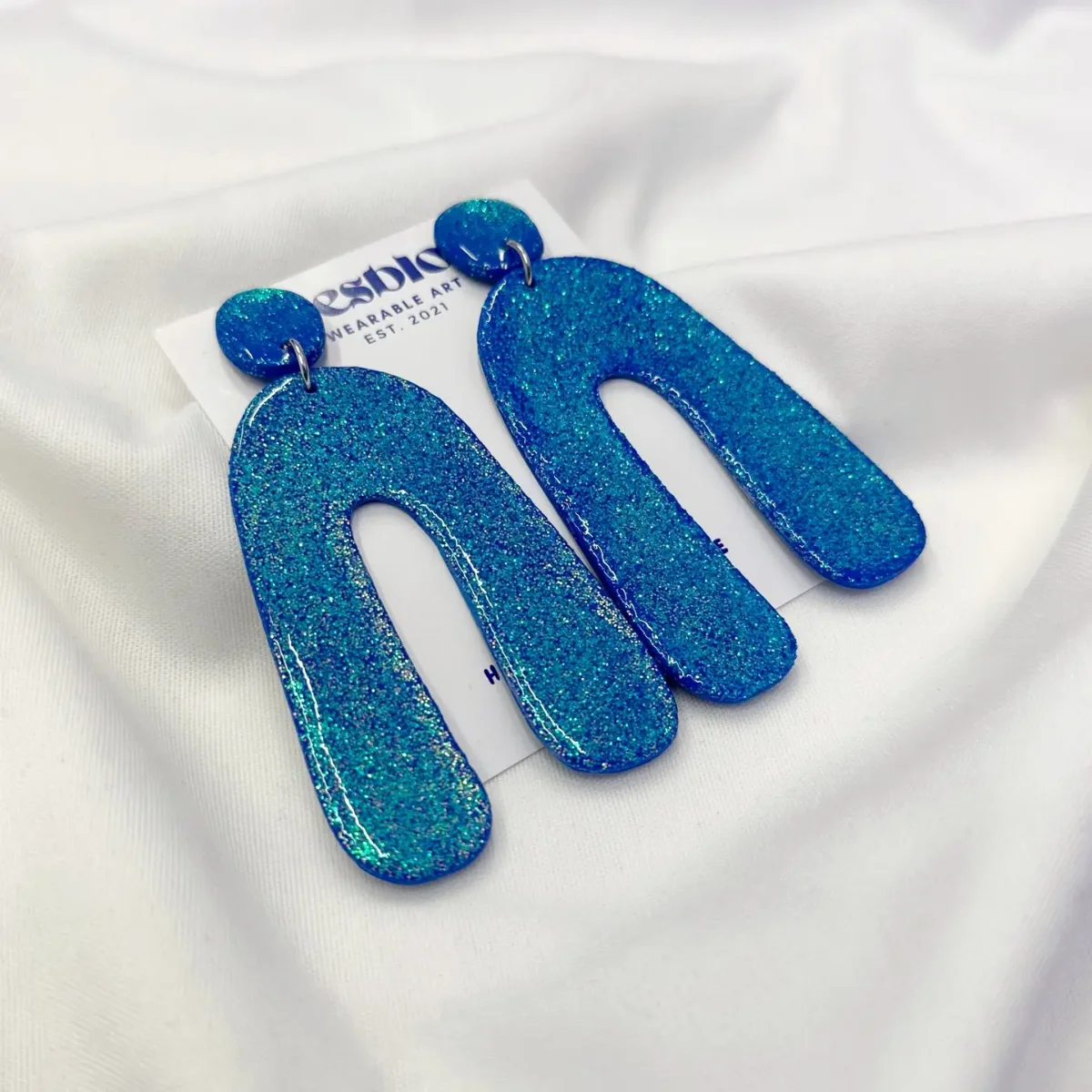 Ohrringe Fimo Glitzer: Tropfenförmige blaue Ohrringe mit Glitzereffekt auf weißem Stoff