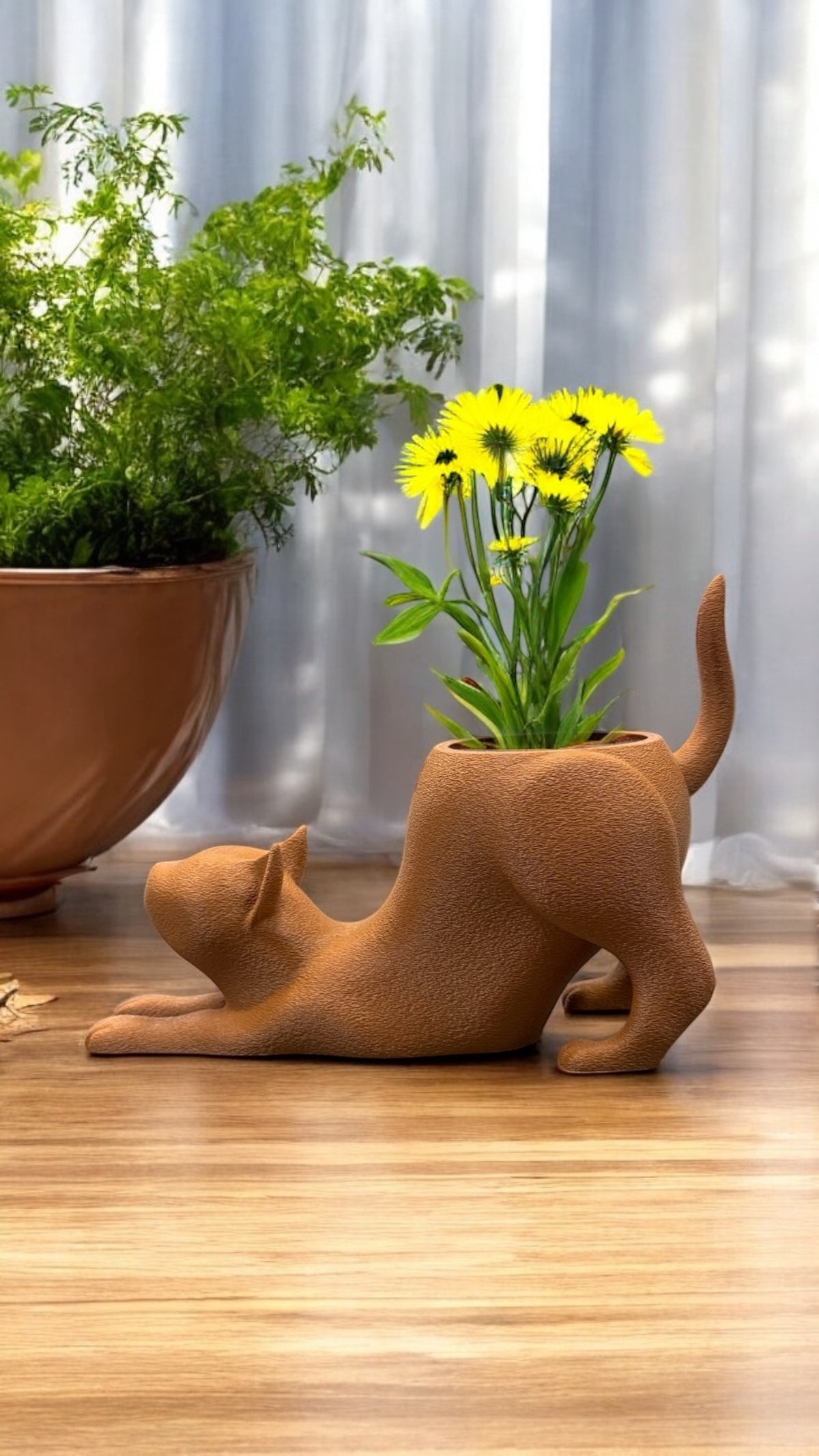 Blumentopf Katze in Braun, gestreckte Pose, mit gelben Blüten bepflanzt, von vorne auf Holzboden