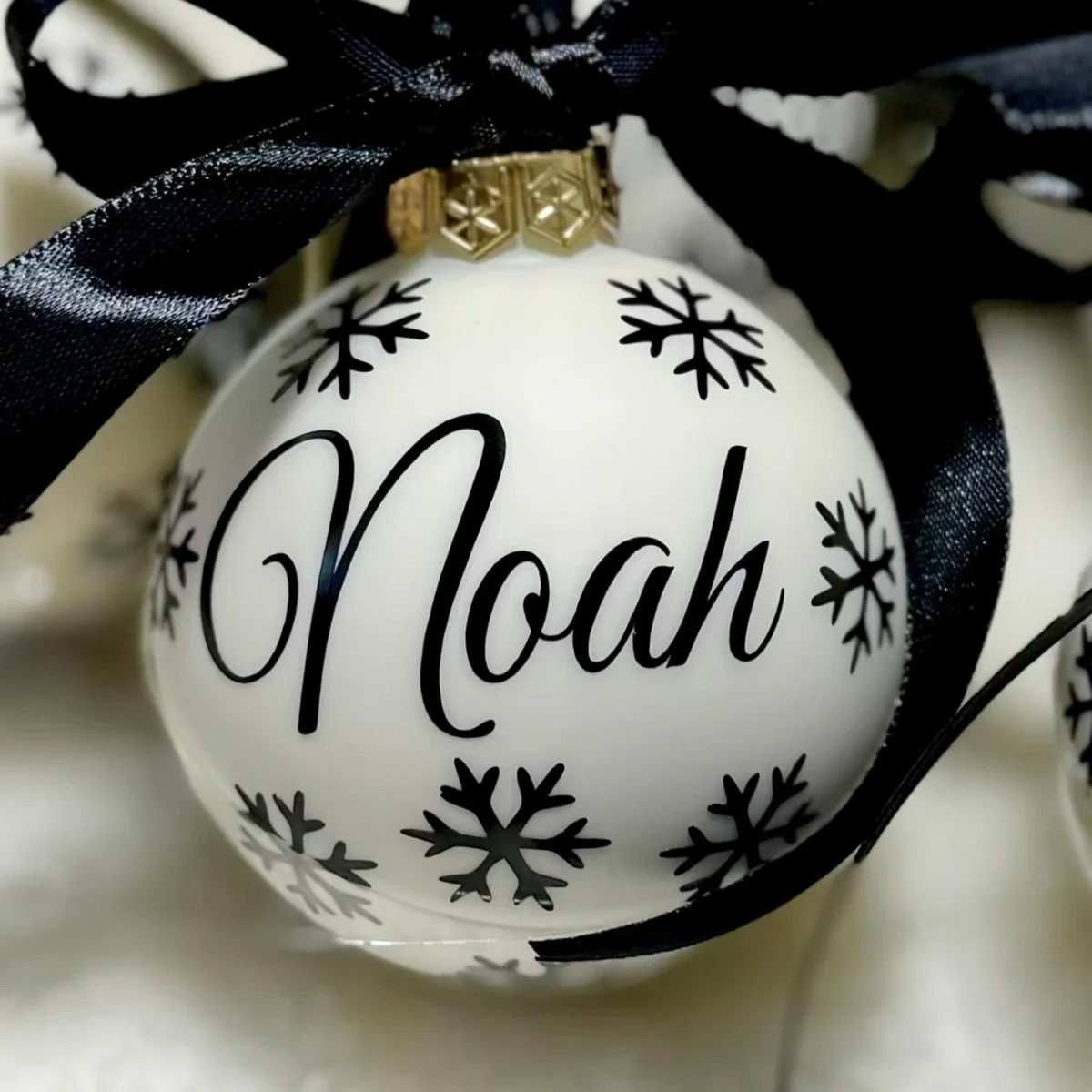 Weiße Glaskugel mit schwarzen Schneeflocken und dem Namen „Noah
