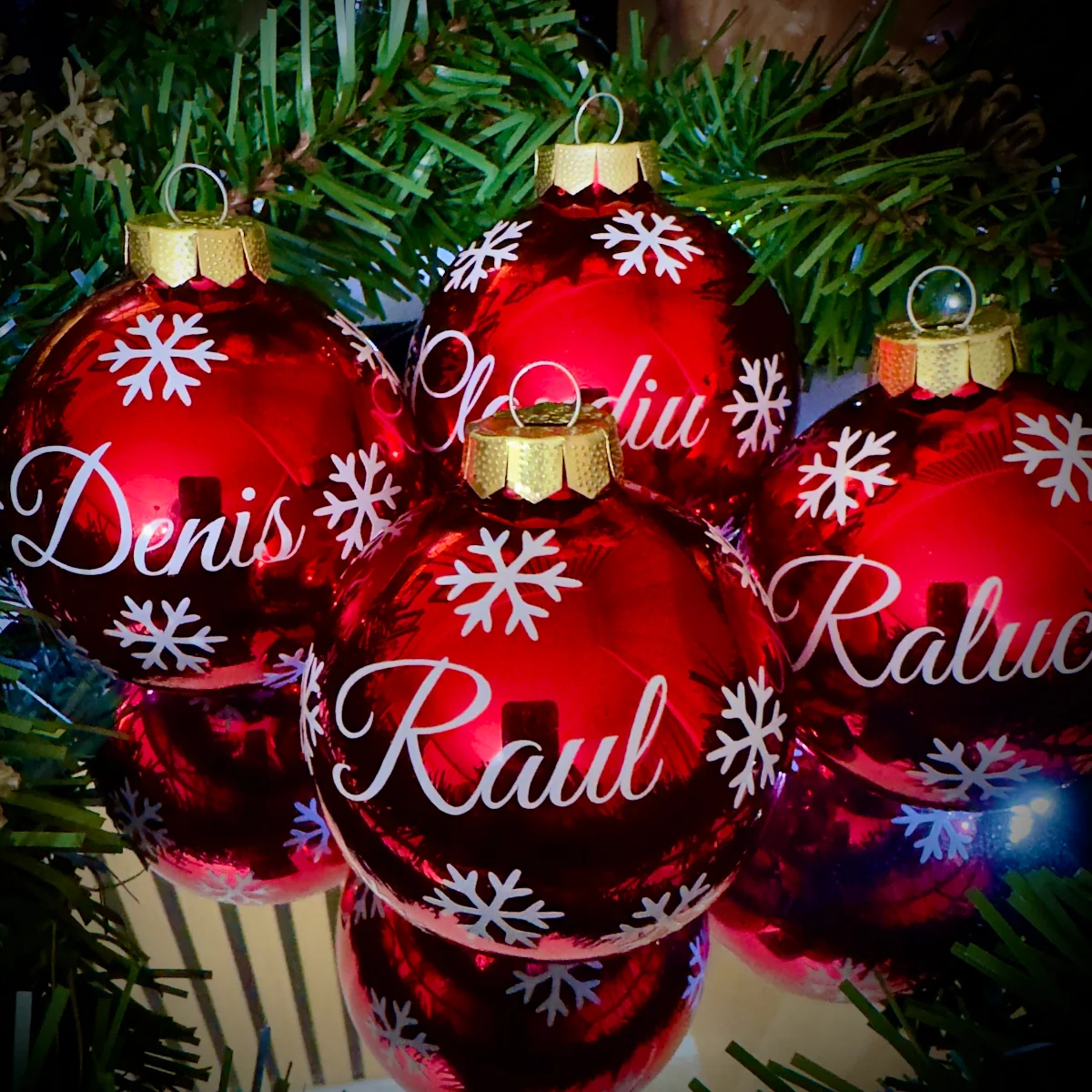 Rote Weihnachtskugeln mit weißen Schneeflocken und Namen wie Raul und Denis am Christbaum