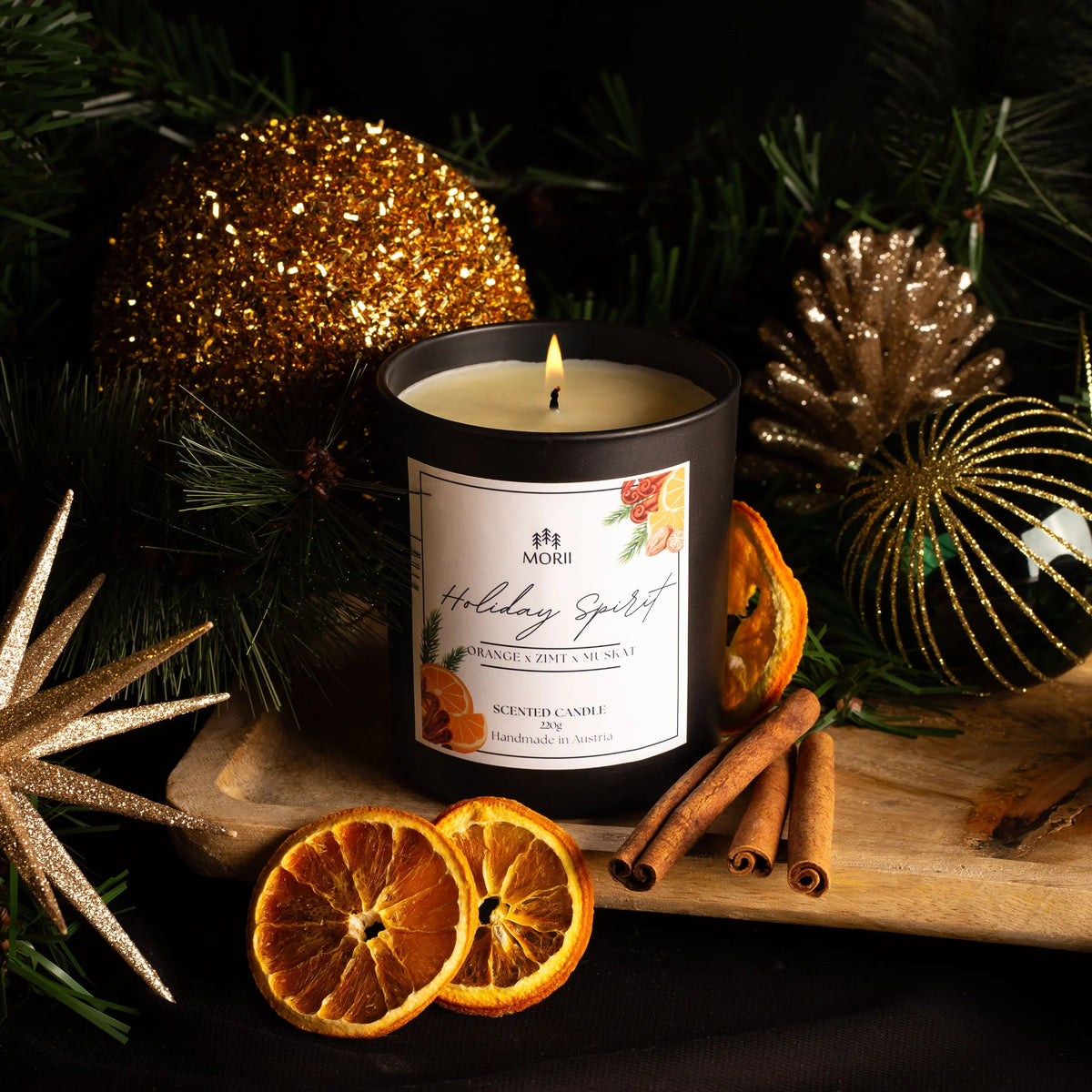 Duftkerze Weihnachten: Schwarze Kerze mit brennender Flamme, umgeben von getrockneten Orangenscheiben, Zimtstangen und…