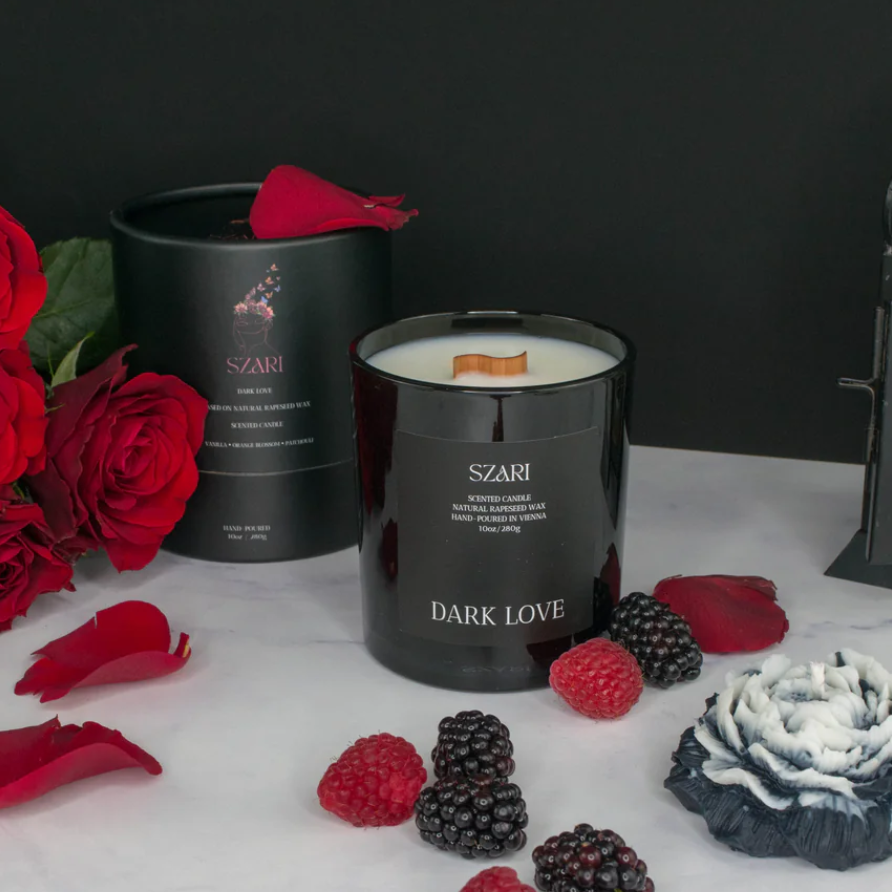 Duftkerze Beeren: Schwarze Kerze mit Holzdocht und Wachsfluss, umgeben von roten Rosen, Himbeeren und Brombeeren auf Marmor.