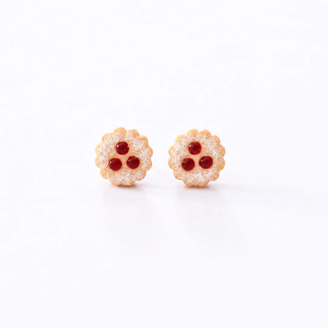 Zwei kleine Ohrstecker in Form von Linzer Augen, goldbraun gebacken mit roter Marmeladenfüllung, auf weißem Hintergrund…