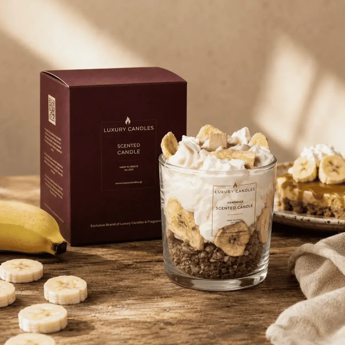 Duftkerze Sojawachs mit Bananenscheiben und Kekskrümeln in Glaszylinder, daneben Verpackungsbox und frische Banane