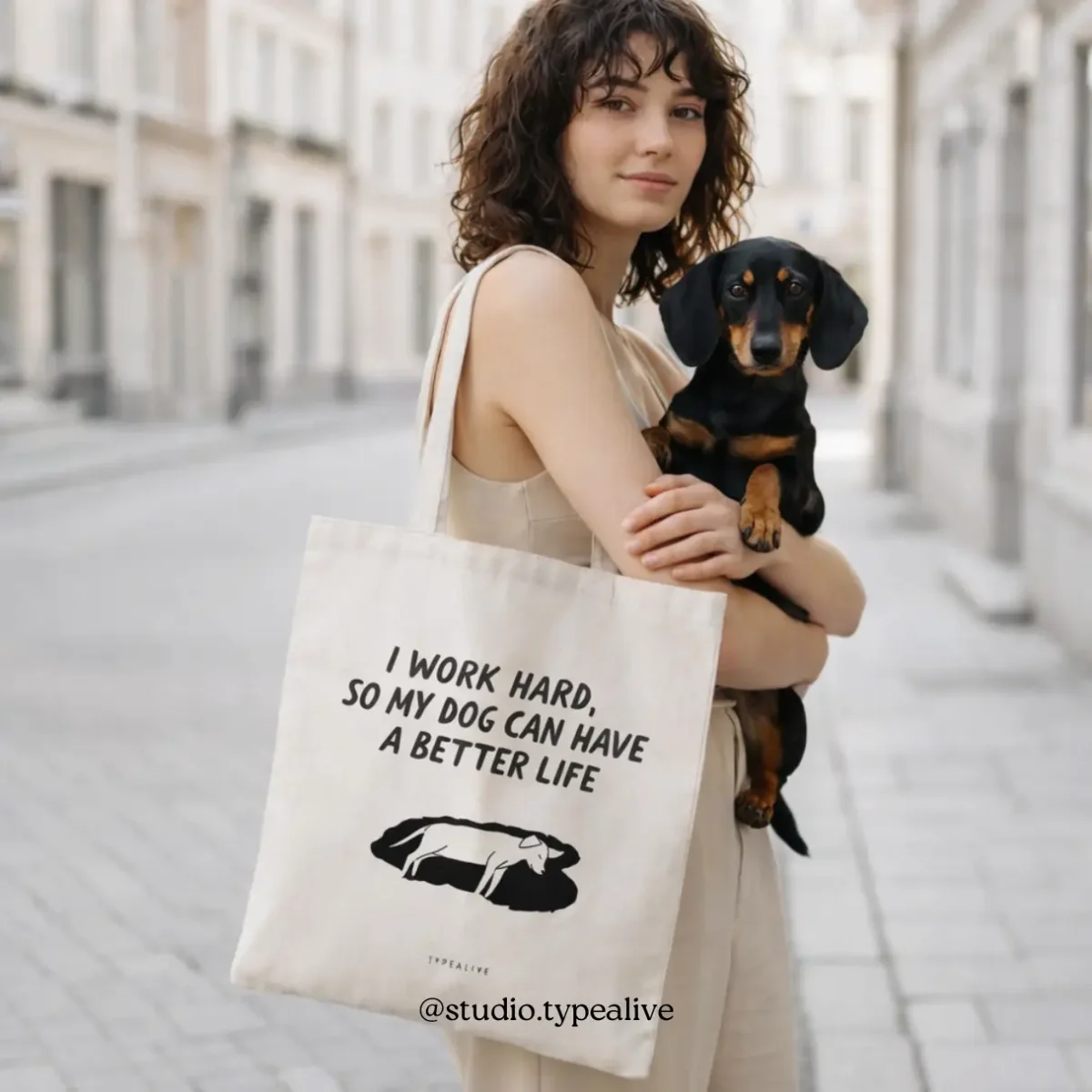 Frau mit schwarzem Dackel trägt beige Baumwolltasche mit schwarzem Spruchdruck auf der Straße