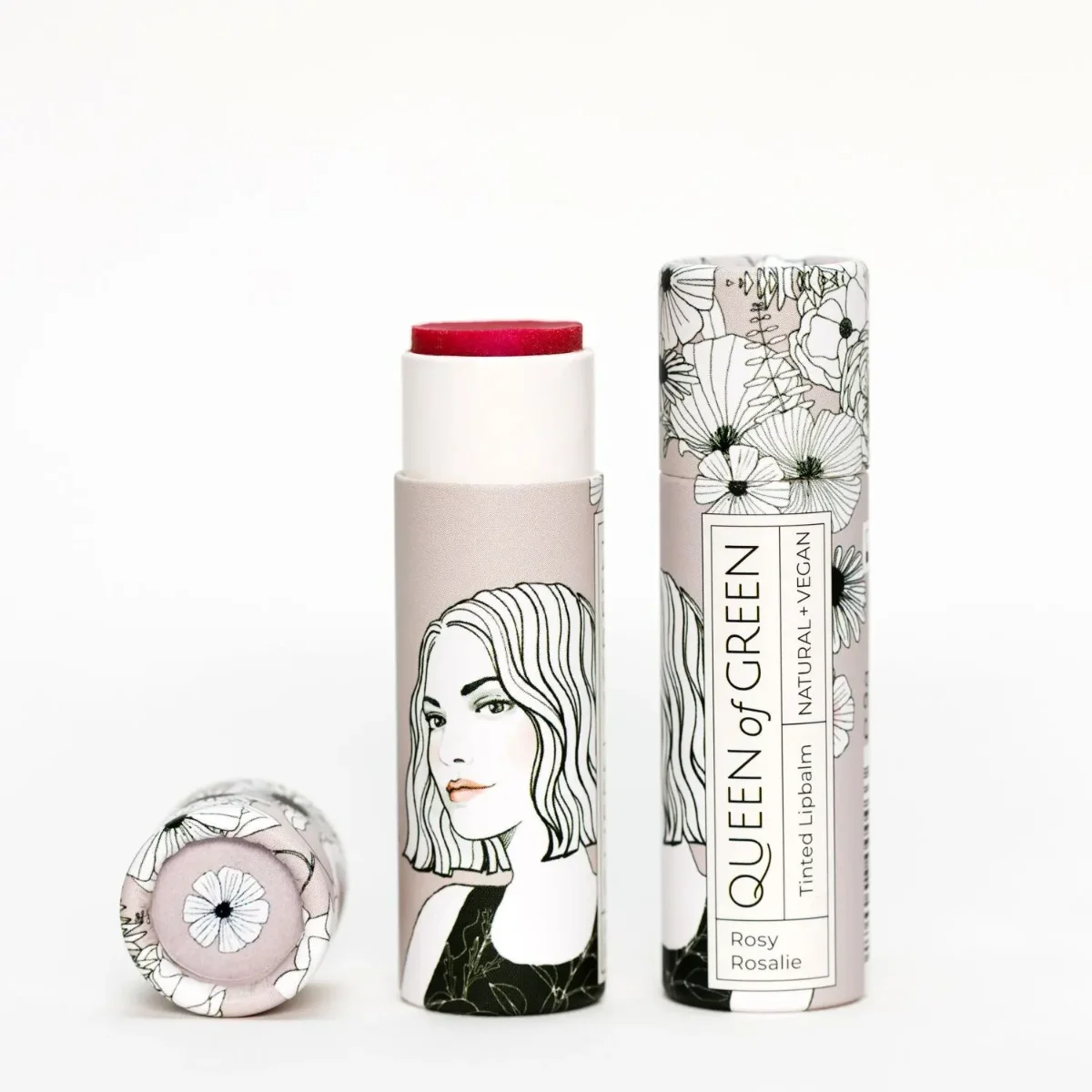 Getönter Lippenbalsam im Kartonhülle mit Frauenporträt und Blumenmuster, Stift ausgedreht, rosa Farbe sichtbar, daneben die…