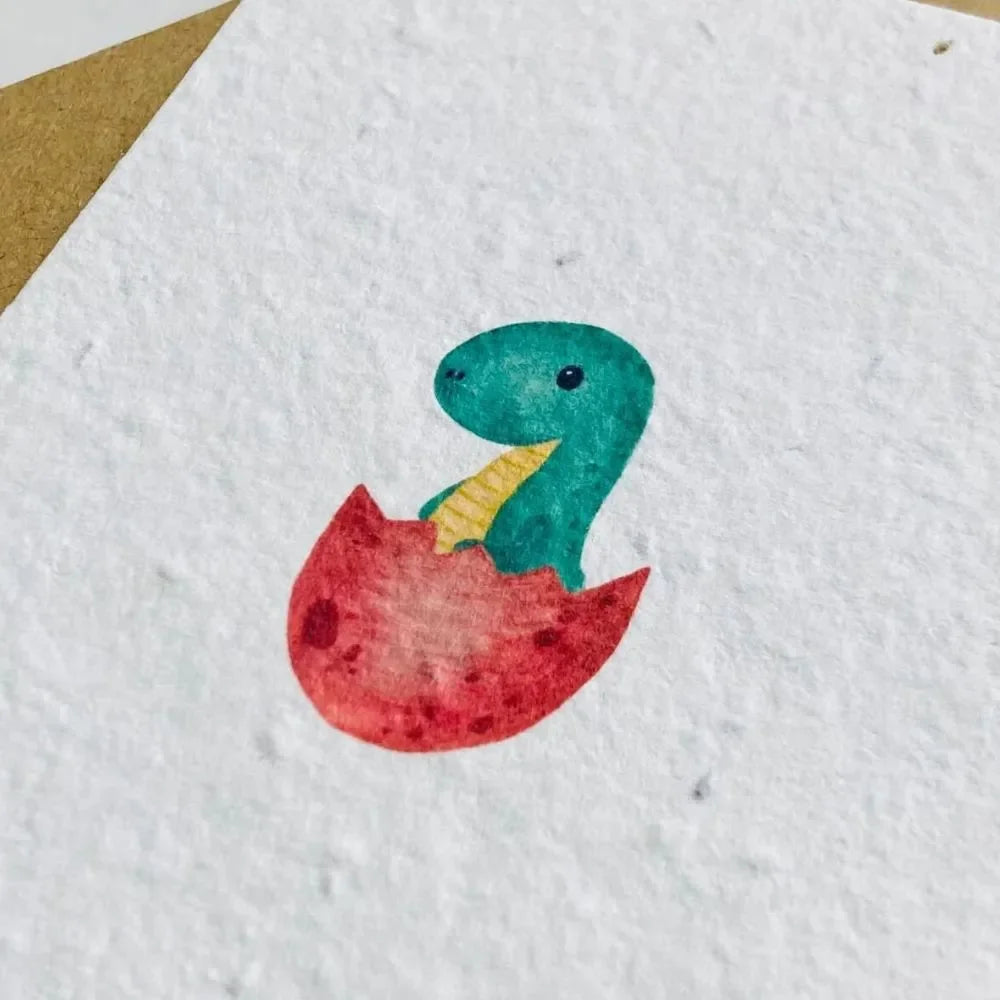 Handgemalter Dinosaurier in Türkis und Rot, schlüpft aus roter Eierschale auf strukturiertem Saatpapier