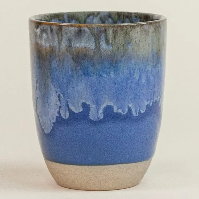 Cappuccino Tasse Keramik: blaue Glasur mit hellen Schlieren, unten naturfarbener Steinzeug-Fuß, Seitenansicht vor hellem…