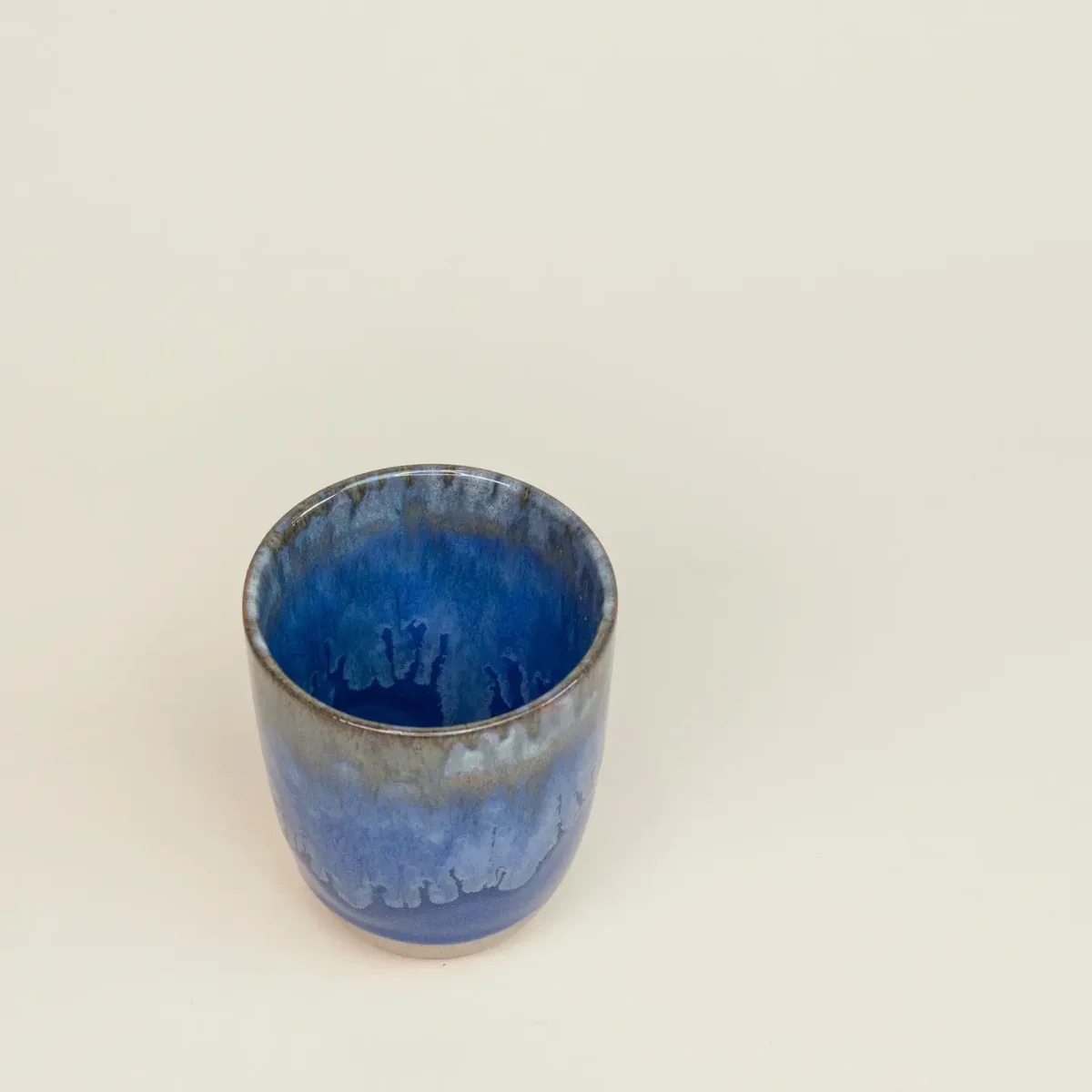 Blaue Keramiktasse ohne Henkel, von oben leicht schräg fotografiert; innen dunkelblau glasiert, außen zum Boden hin heller…