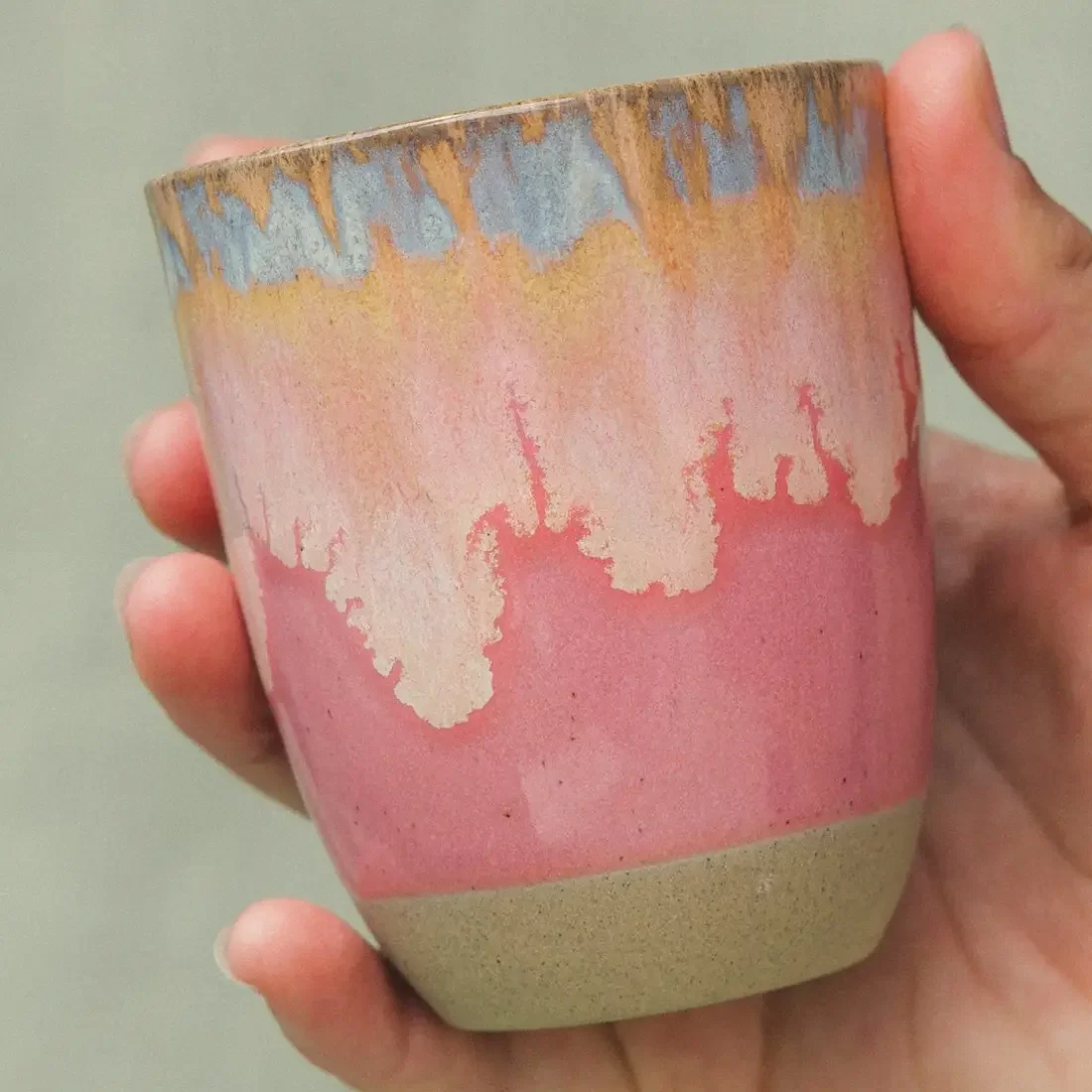 Cappuccino Tasse Keramik: Hand hält eine Tasse mit rosa Glasur, die nach oben in Beige und Hellblau übergeht, unten…