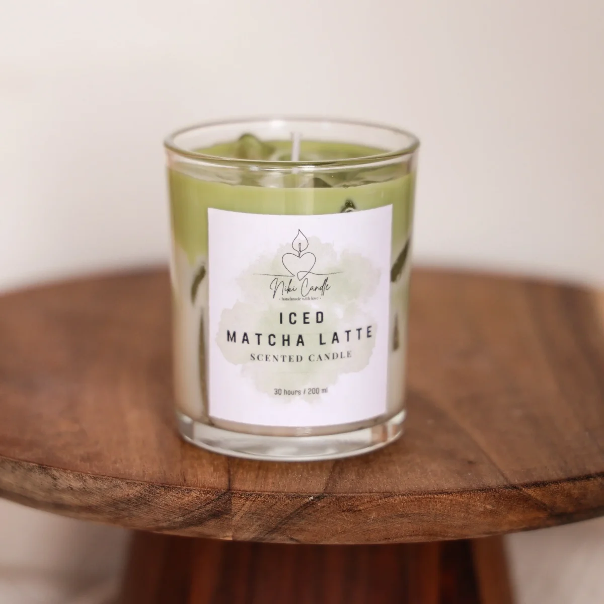 Duftkerze Matcha Latte in Glaszylinder mit grünem Wachs und weißem Label, auf Holzschale
