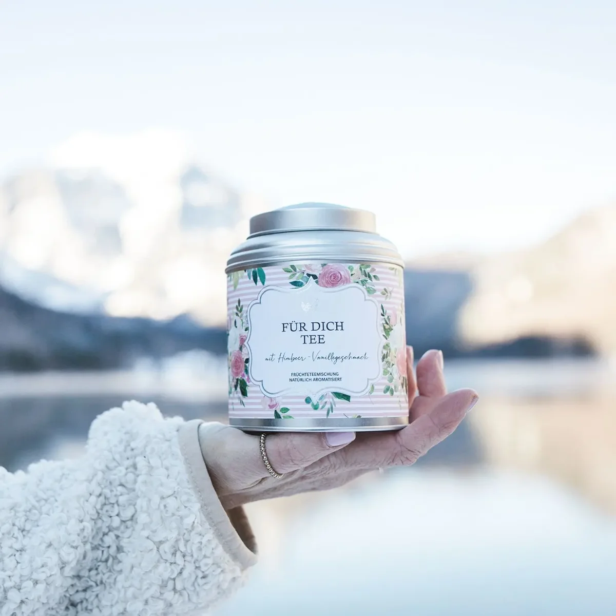 Teebehälter mit Blumenmotiv in einer Hand, im Hintergrund unscharfe Winterlandschaft