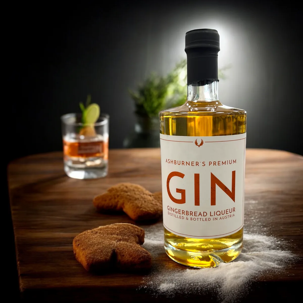 Ashburner's Gingerbread Gin Flasche mit schwarzem Verschluss neben Lebkuchen-Keksen auf Holzbrett, im Hintergrund ein…