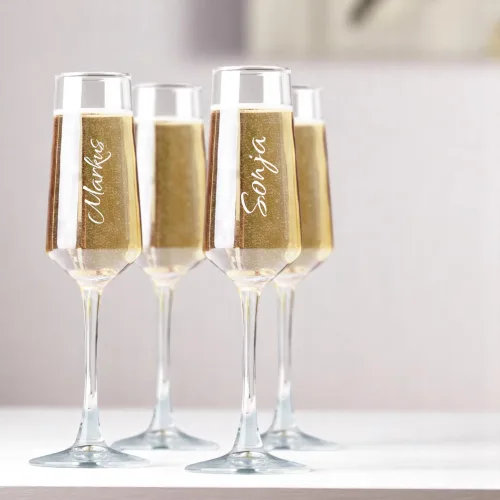 Vier mundgeblasene Sektgläser mit Champagner gefüllt, zwei davon mit gravierten Namen auf der Glasfläche, nebeneinander…