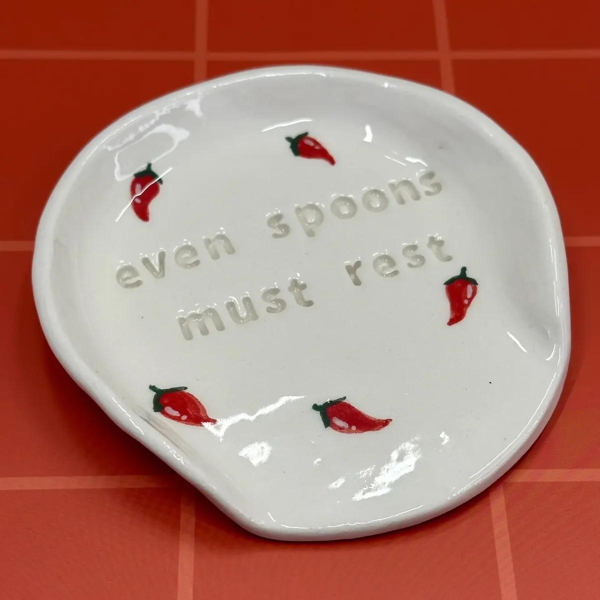 Löffelablage aus weißer Keramik mit Schriftzug „even spoons must rest