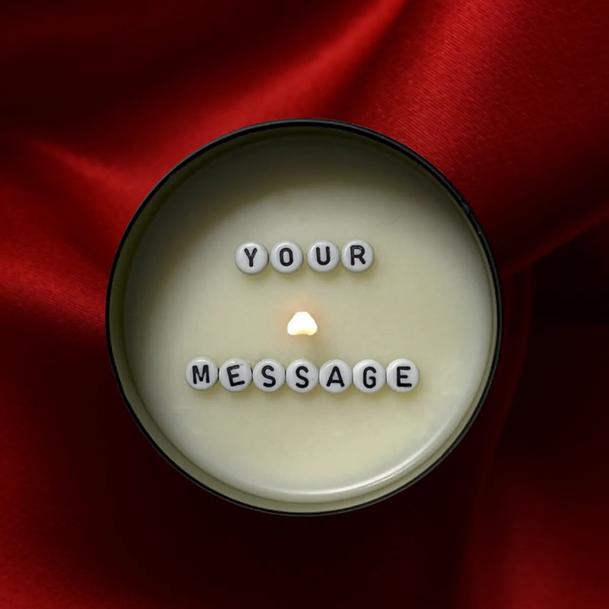 Brennende Kerze von oben, cremefarbenes Wachs mit weißen Buchstabenperlen, die "YOUR MESSAGE" bilden, auf rotem Untergrund.