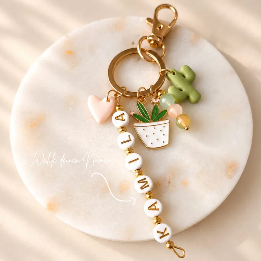 Schlüsselanhänger mit goldenem Ring, weißen Buchstabenperlen mit Namen, grünem Kaktus, Topfpflanze, rosa Herz und…