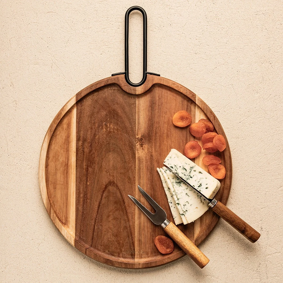 Rundes Holzbrett mit schwarzem Griff, belegt mit Blauschimmelkäse, Aprikosen und zwei Edelstahlmessern mit Holzgriffen