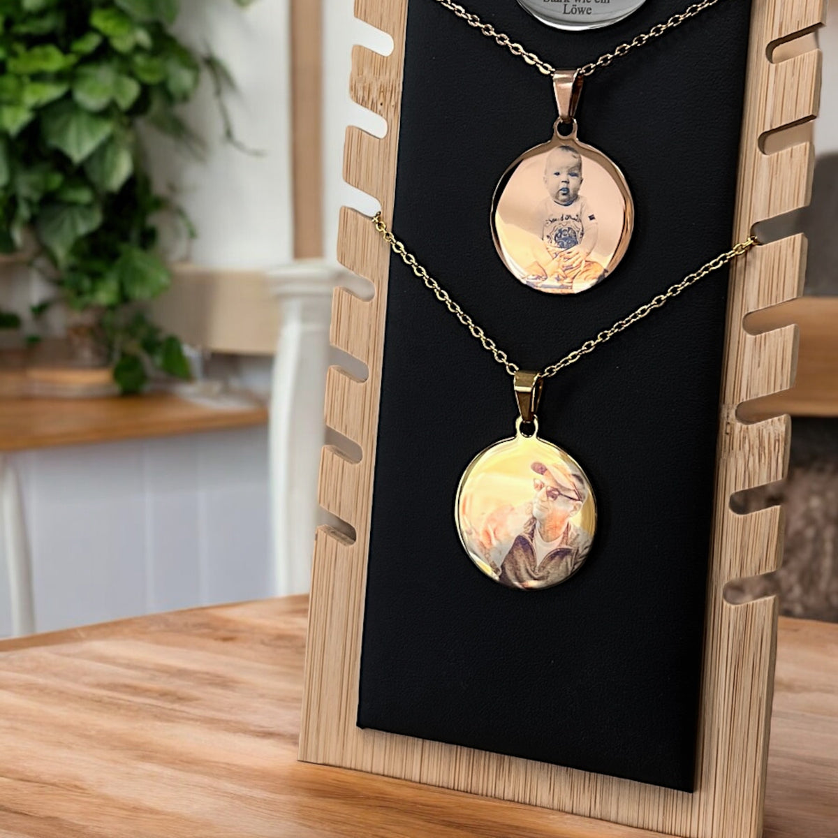 Zwei runde Edelstahl-Anhänger mit Fotogravuren an silberner Kette, auf schwarzem Präsentationsbrett aus Holz und Stoff.