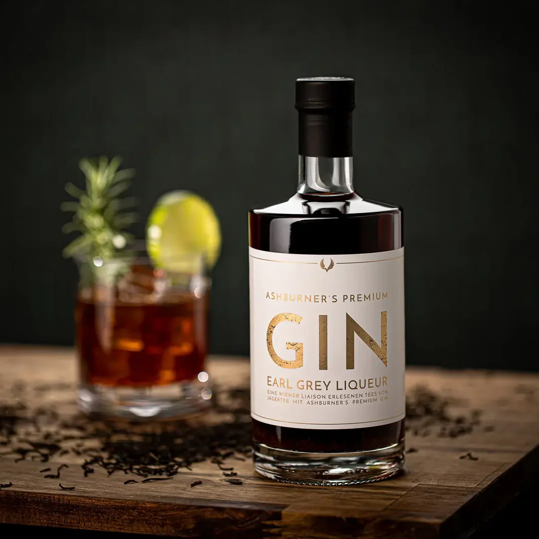 Earl Grey Gin Flasche mit schwarzem Etikett auf Holzoberfläche, daneben Glas mit dunklem Getränk und Zitronenscheibe