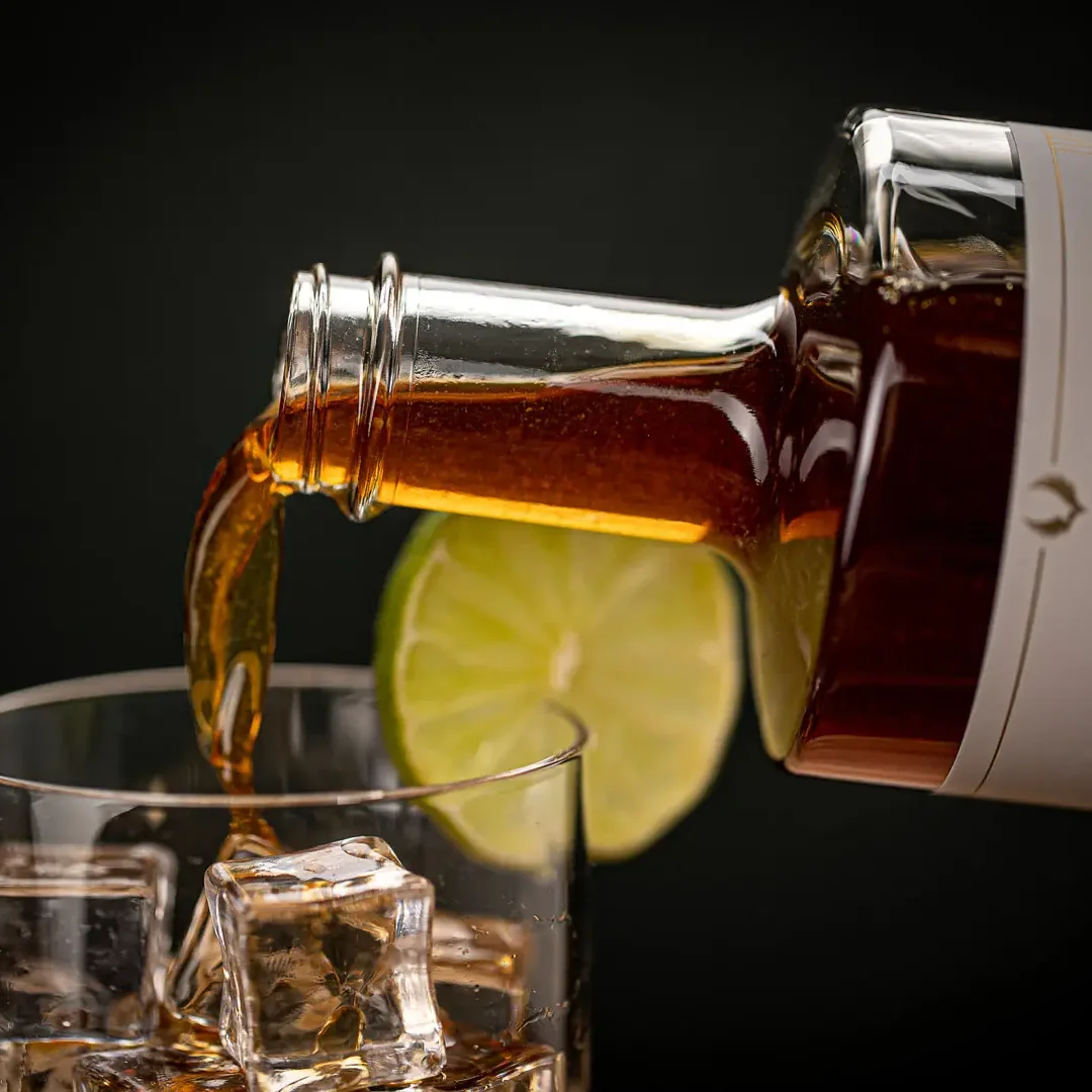 Bernsteinfarbener Gin wird aus einer Flasche in ein Glas mit Limettenscheibe und Eiswürfeln gegossen.